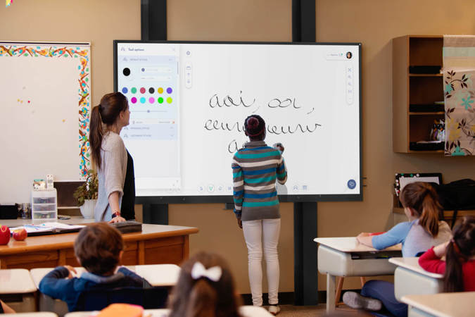 A student types on an i3TOUCH interactive whiteboard under the supervision of her teacher.