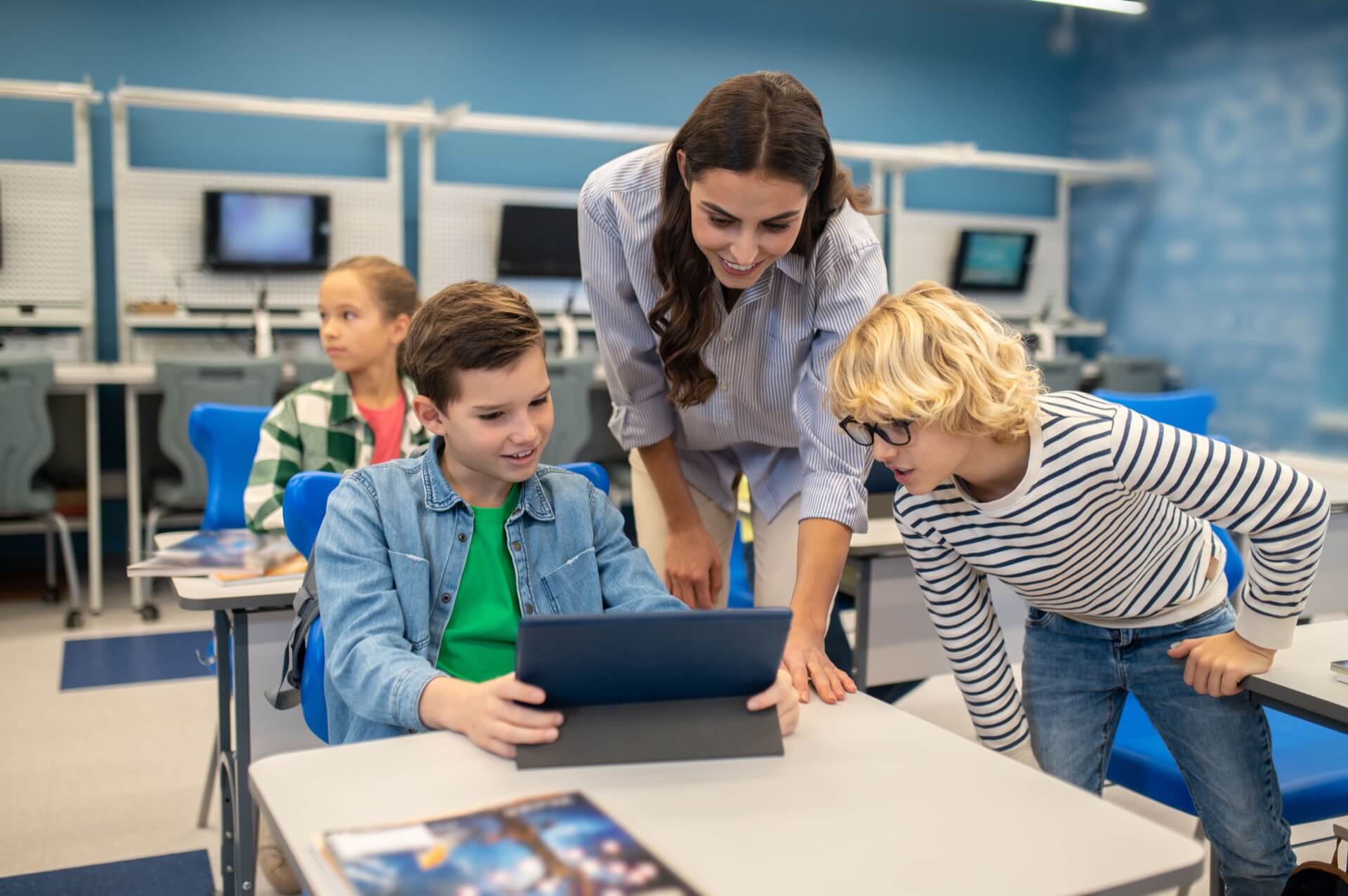 Two students showing some classwork to the teacher using a tablet.