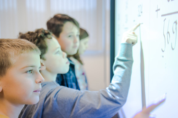 Vier Kinder, die Matheaufgaben auf einem interaktiven Whiteboard erledigen.